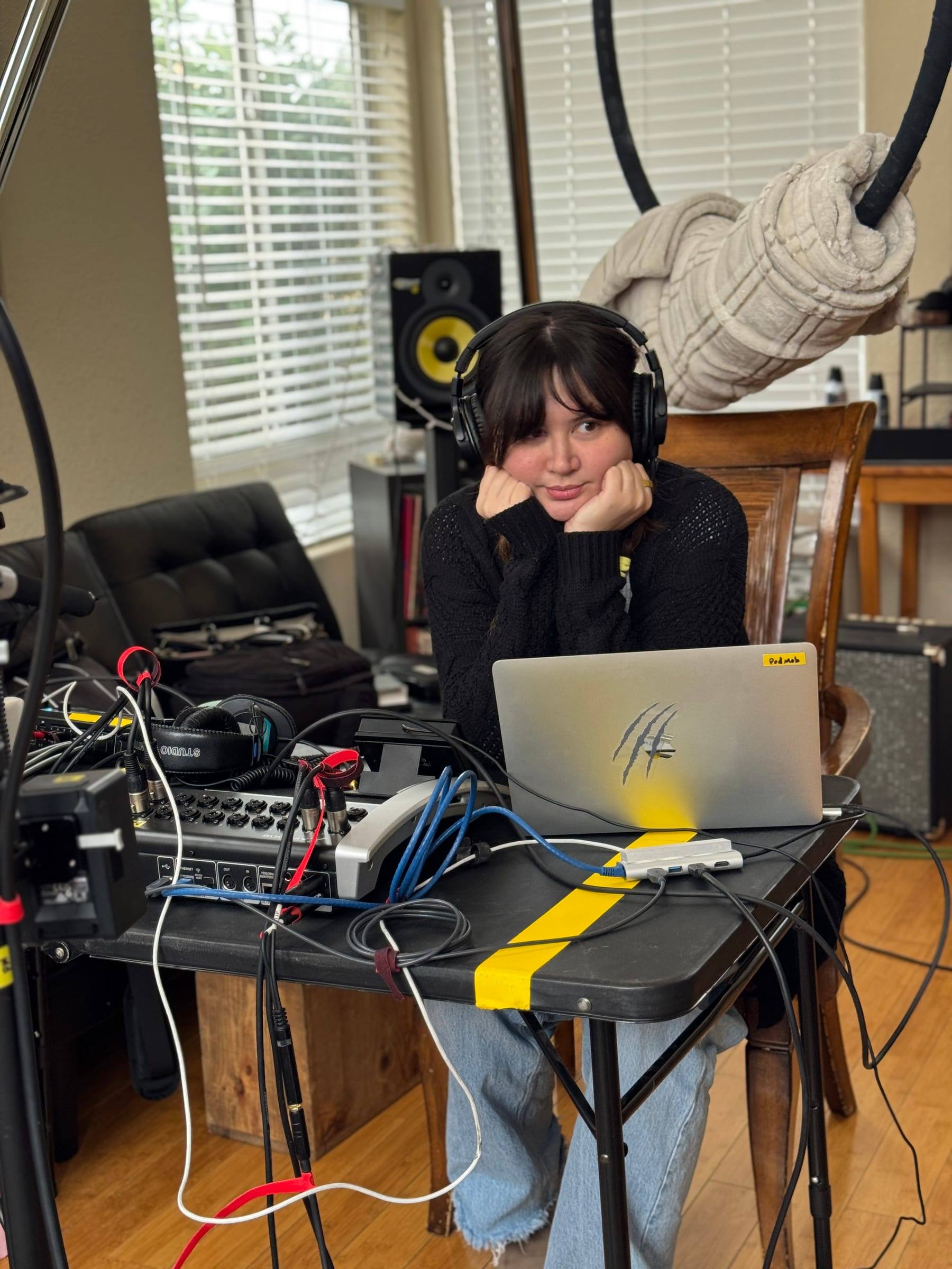 A podcast host in headphones at a laptop during a home recording