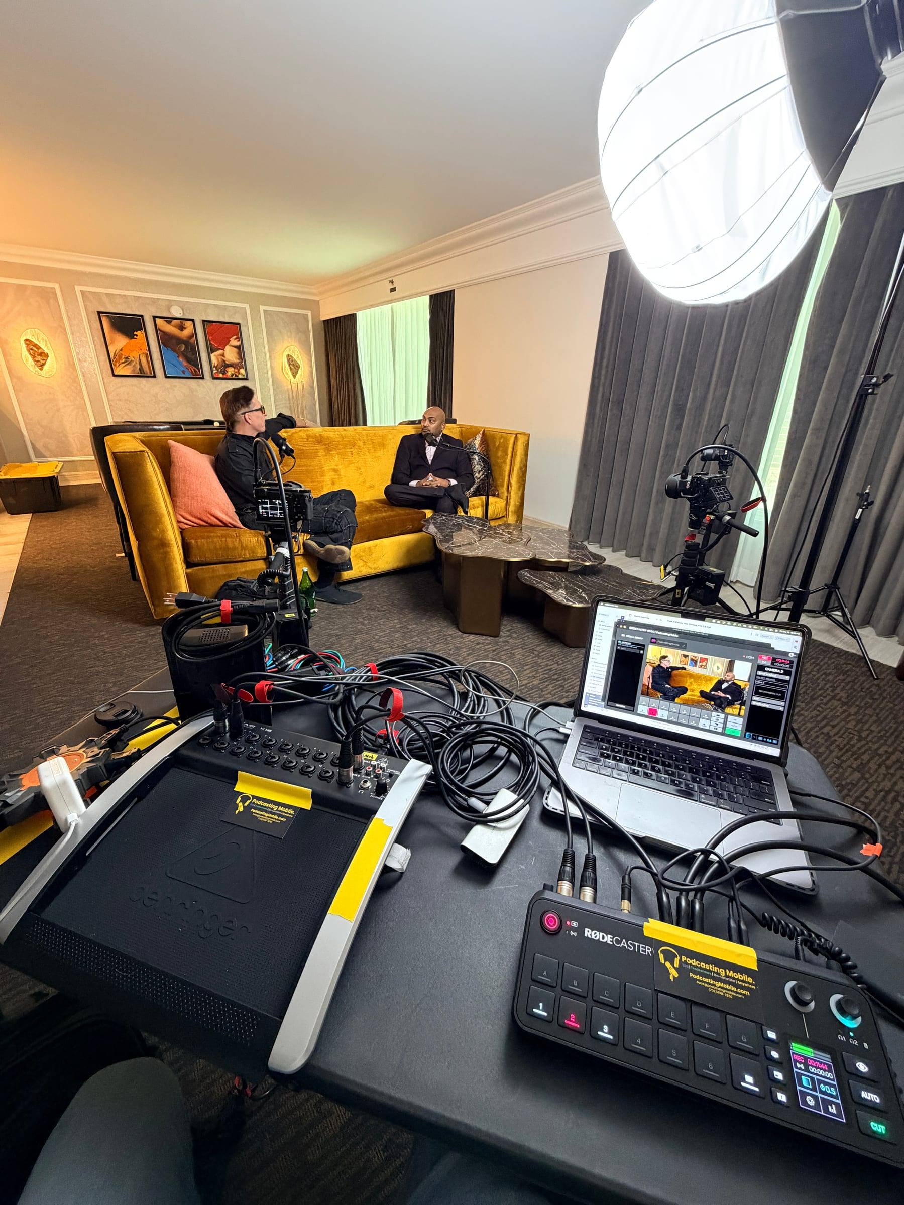 A Las Vegas hotel suite turned into a podcast set, with hosts on a gold sofa and cameras and the engineering desk in front