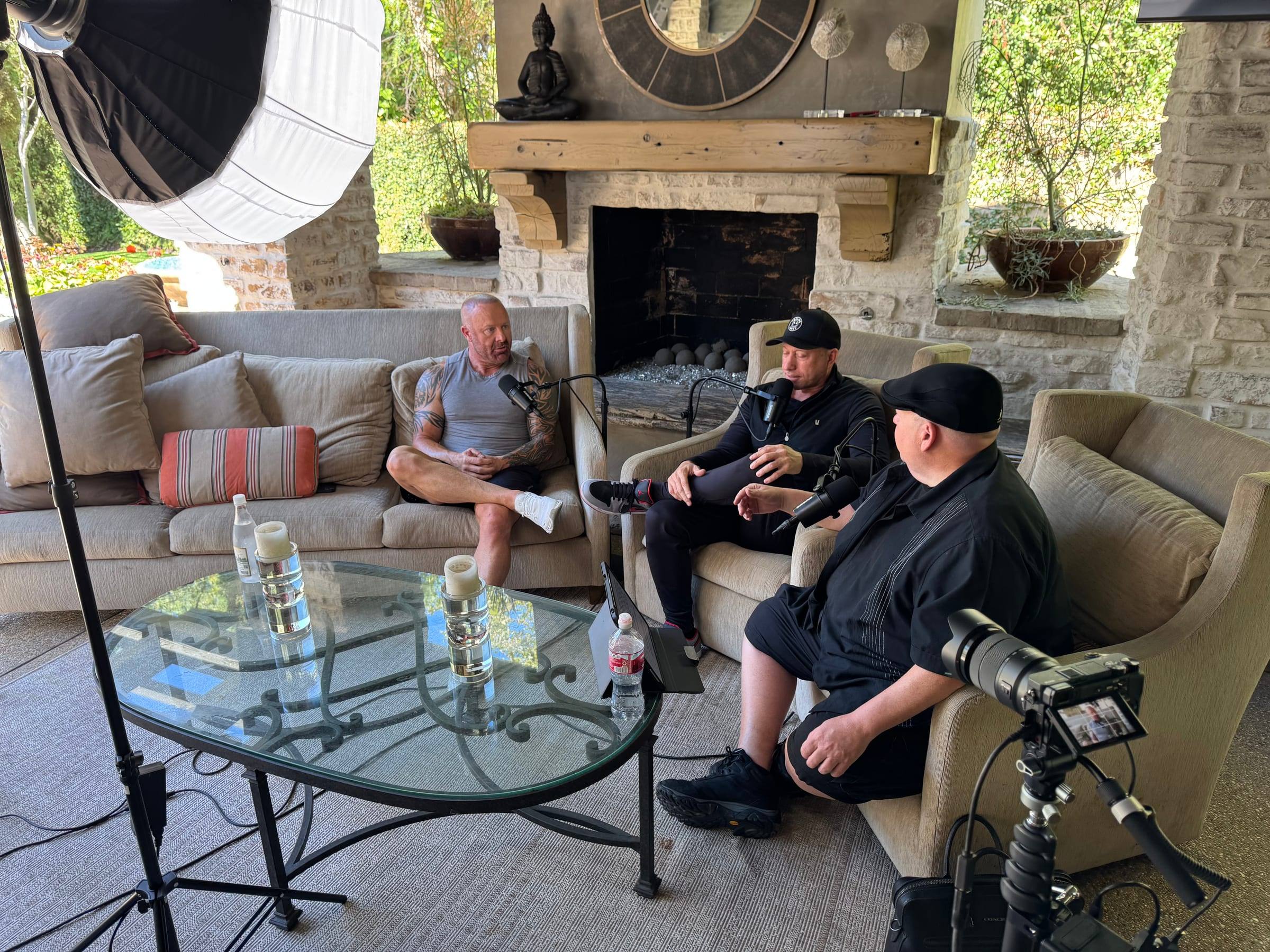 Hosts and a guest recording on a backyard patio set, with cameras in the foreground