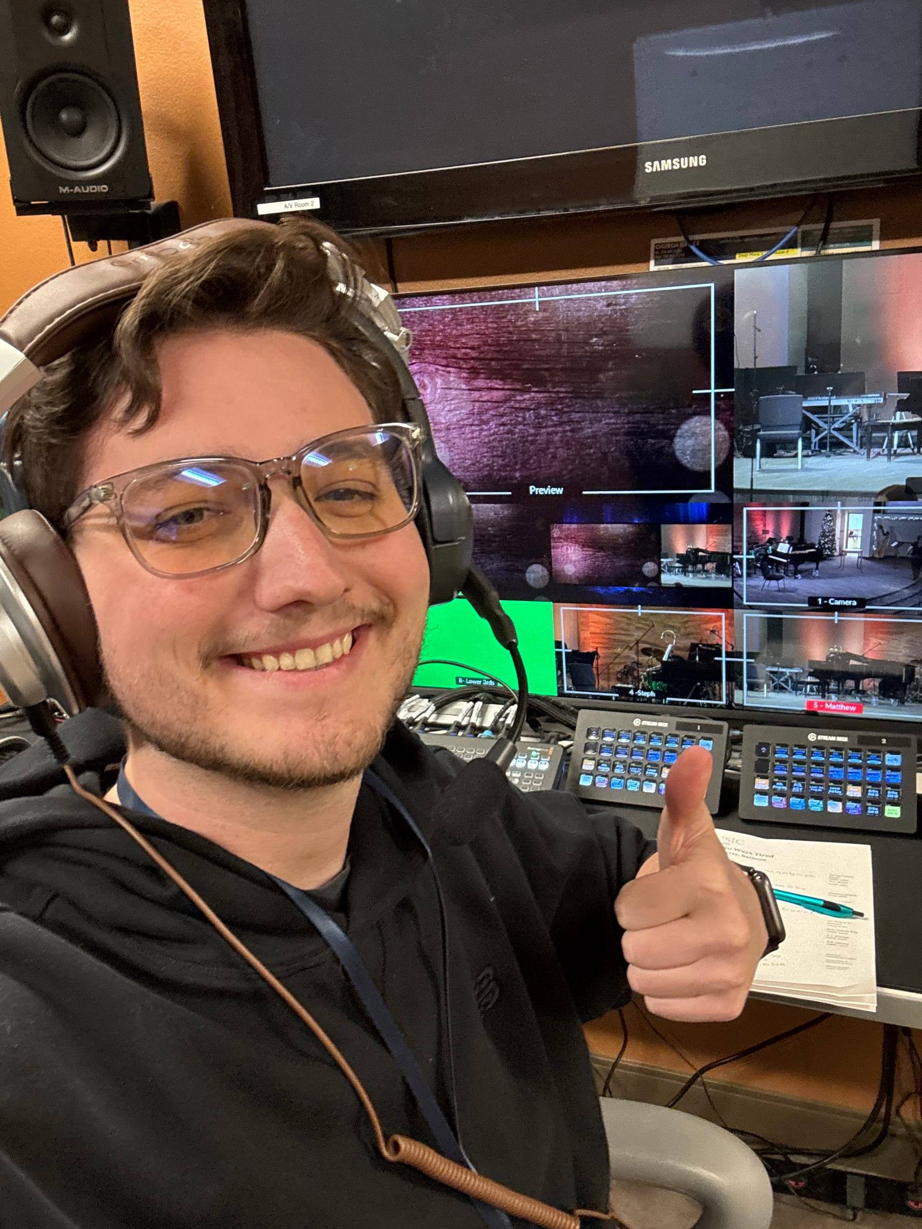 Travis Flesher smiling in headphones in front of a live production desk